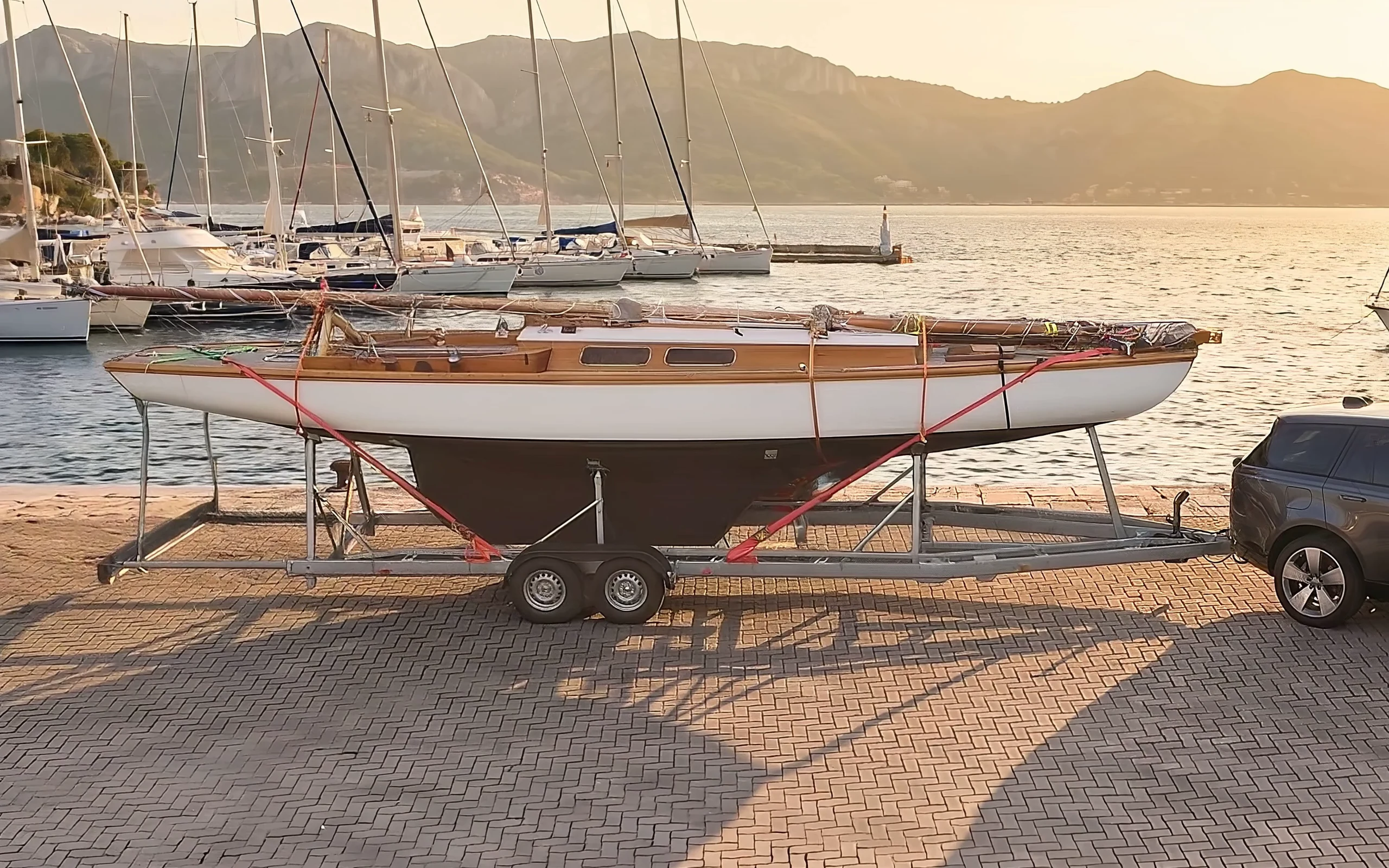Klassisches Segelboot mit roten Gurten auf einem Bootsanhänger von bunnefeld an einer Hafenmole im Abendlicht